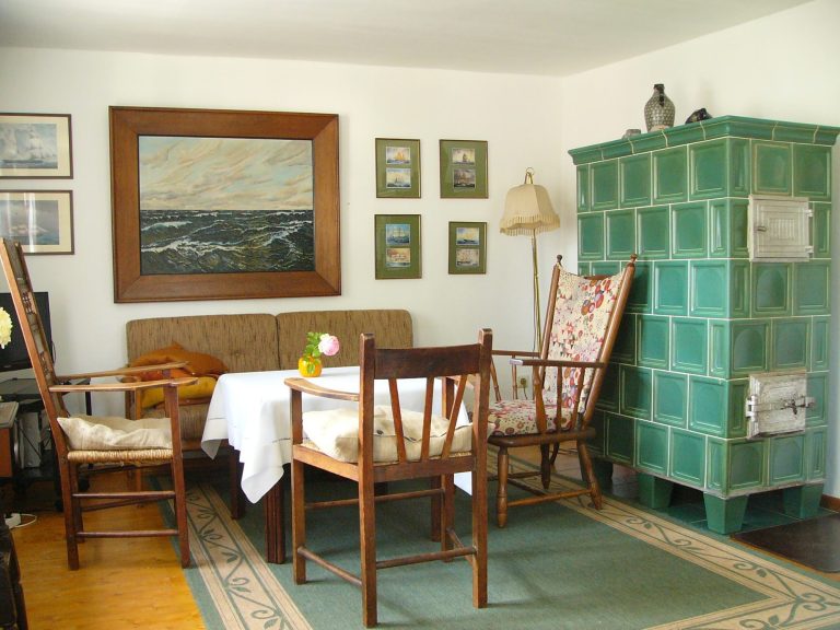 Gemütlicher Raum mit einem Tisch, Stühlen, einem Kachelofen und mehreren Bildern an der Wand.