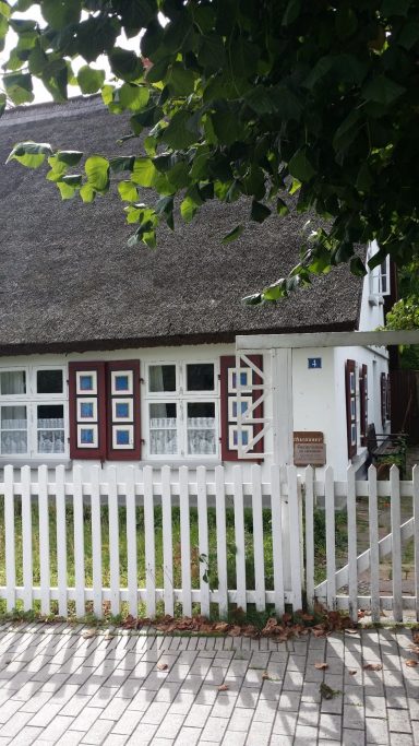 Reetdachhaus mit weißen Wänden und bunten Fenstern, umgeben von einem weißen Zaun.