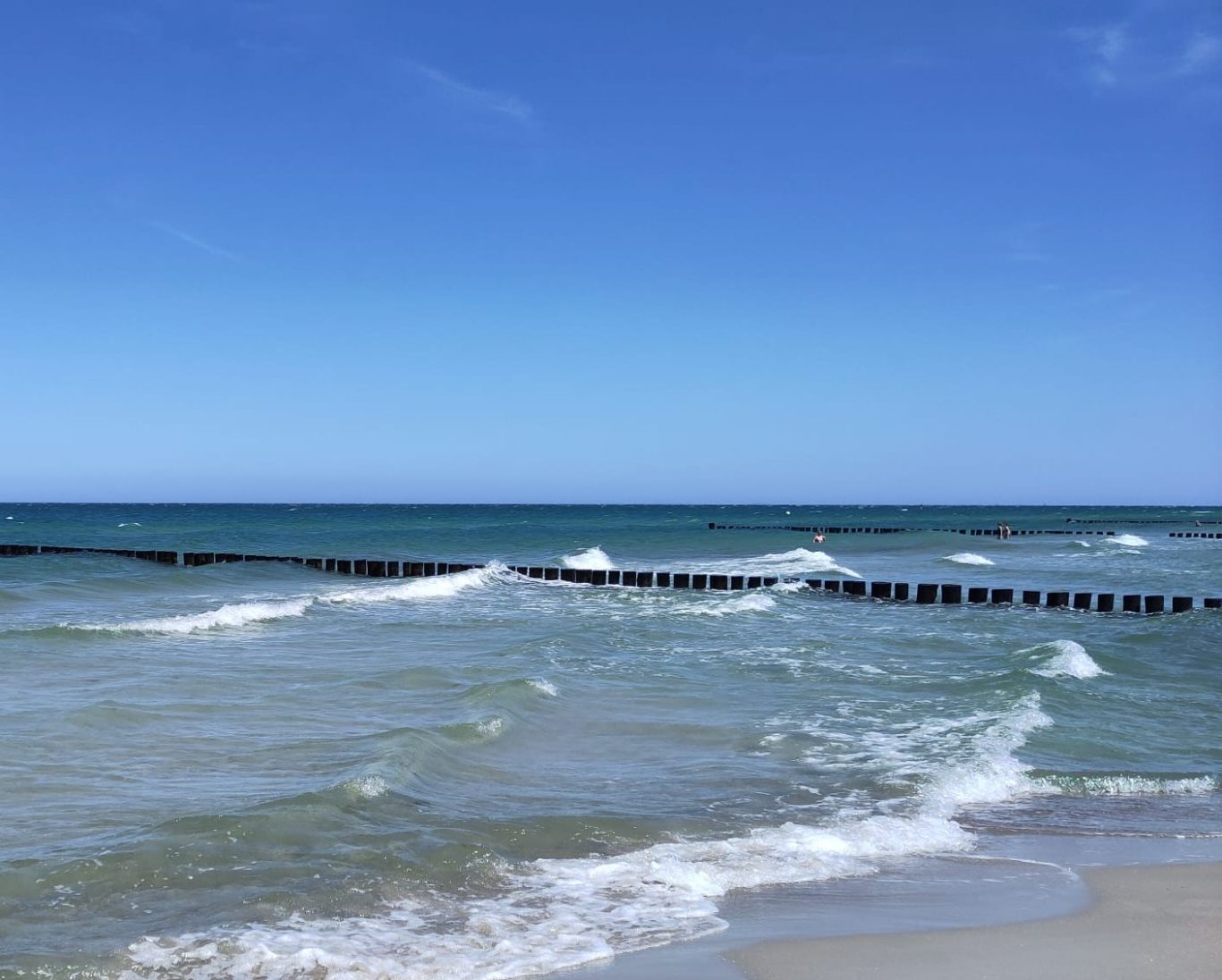 Strand mit sanften Wellen und einem klaren blauen Himmel.