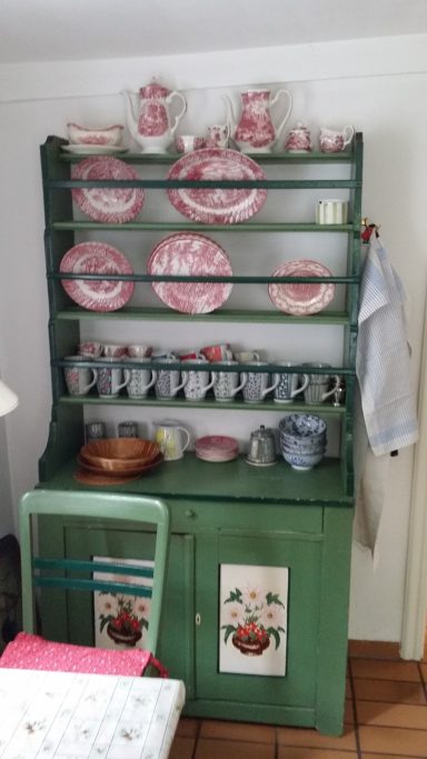 Grüner Küchenschrank mit Geschirr und Tassen in rot-weißen Mustern.