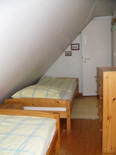Schlafzimmer mit zwei Betten, Holzmöbeln und einer Tür unter einer Schräge.