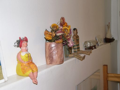 Bunte Dekorationsobjekte, darunter eine sitzende Figur und ein Blumentopf, auf einem Regal.