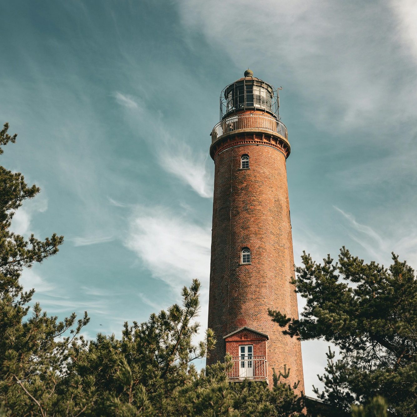 Leuchtturm umgeben von Bäumen unter einem bewölkten Himmel.