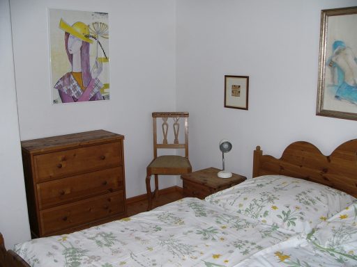 Gemütliches Schlafzimmer mit Bett, Kommode, Stuhl und Bildern an der Wand.