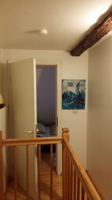Ein Flur mit offenem Türen, Holztreppe und einem Gemälde an der Wand.