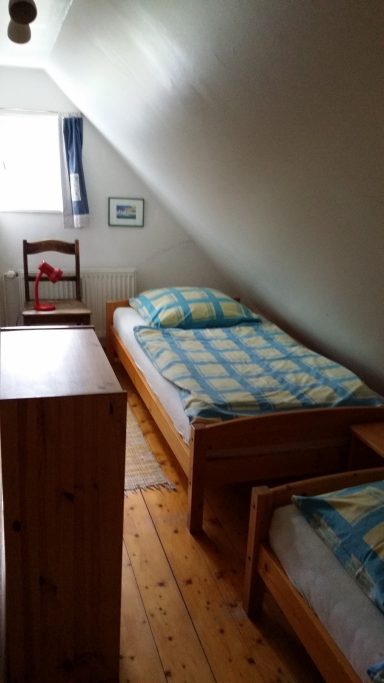 Helles Schlafzimmer mit zwei Einzelbetten, einem Stuhl und einer Kommode.
