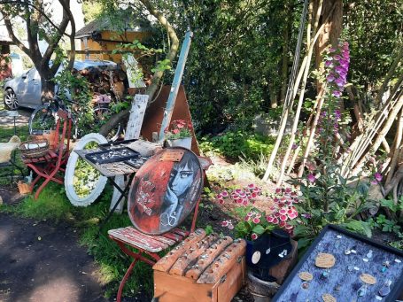 Bunte Gartenlandschaft mit alten Möbeln, Pflanzen und floralen Akzenten.