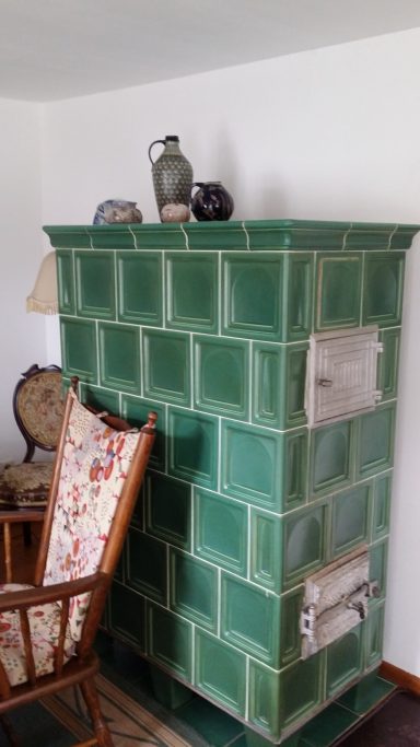 Ein Kachelofen mit grünen Fliesen und Dekoration auf der Oberseite, neben einem Stuhl.