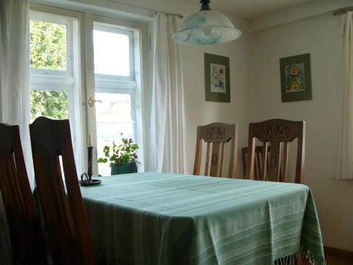 Heller Essbereich mit grünem Tisch, Stühlen und Fenstern mit Vorhängen.