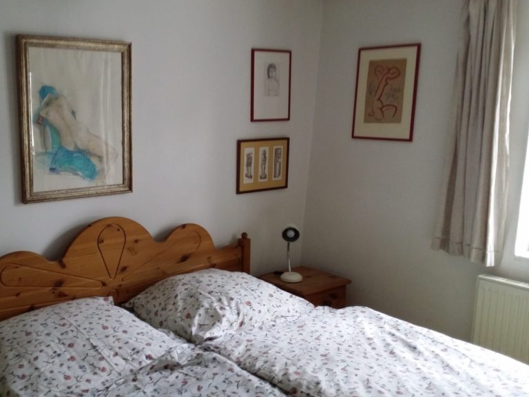 Doppelbett mit gemusterter Bettwäsche in einem hellen Schlafzimmer mit Bildern an der Wand.