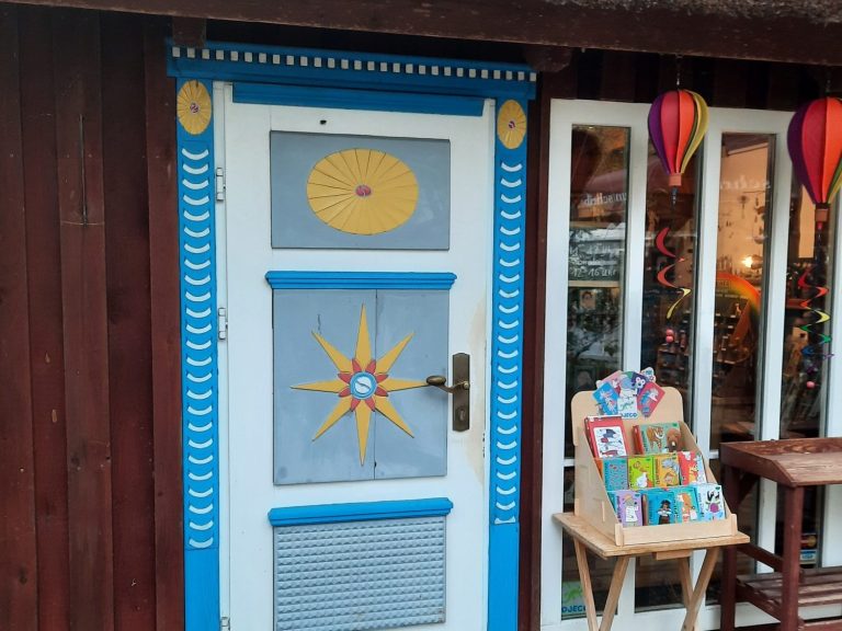 Blaue Tür eines Holzhauses mit bunten Dekorationen und einem Tisch voller Kunsthandwerk uns Spielen.