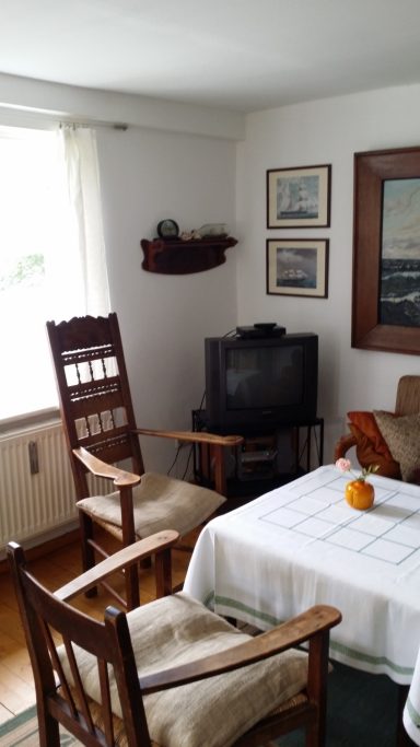 Gemütlicher Raum mit zwei Stühlen, Tisch und Fernseher, an einem Fenster.