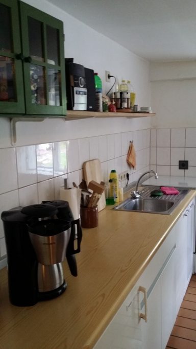 Küchenzeile mit Kaffeemaschine, Spüle und verschiedenen Küchenutensilien.