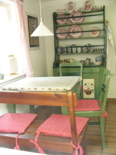 Gemütliche Küche mit einem grünen Regal, einem Holztisch und gepolsterten Stühlen.