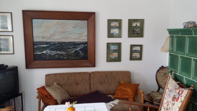 Wohnzimmer mit Sofa, Bildern an der Wand und einem grünen Kachelofen.