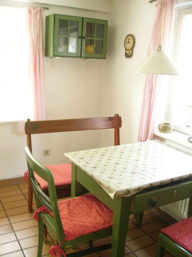 Küche mit grünem Tisch, zwei Stühlen und rosa Vorhängen, helles Licht.